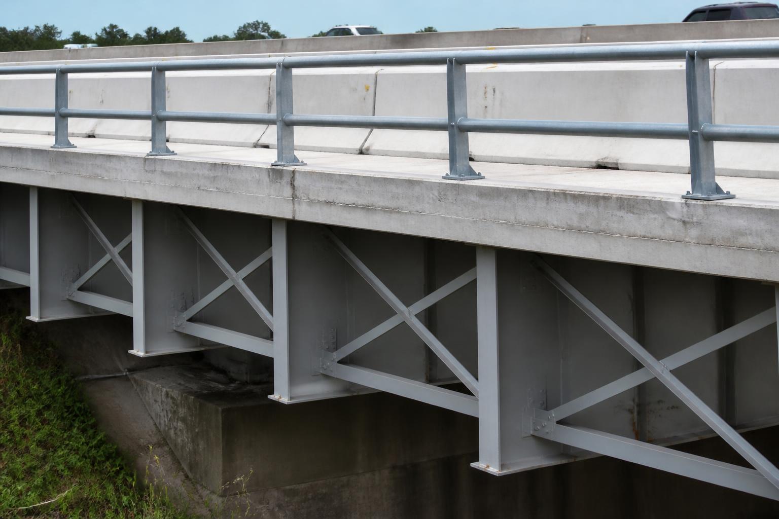Concrete Jersey barrier on top of a bridge deck with steel cross-frames visible below