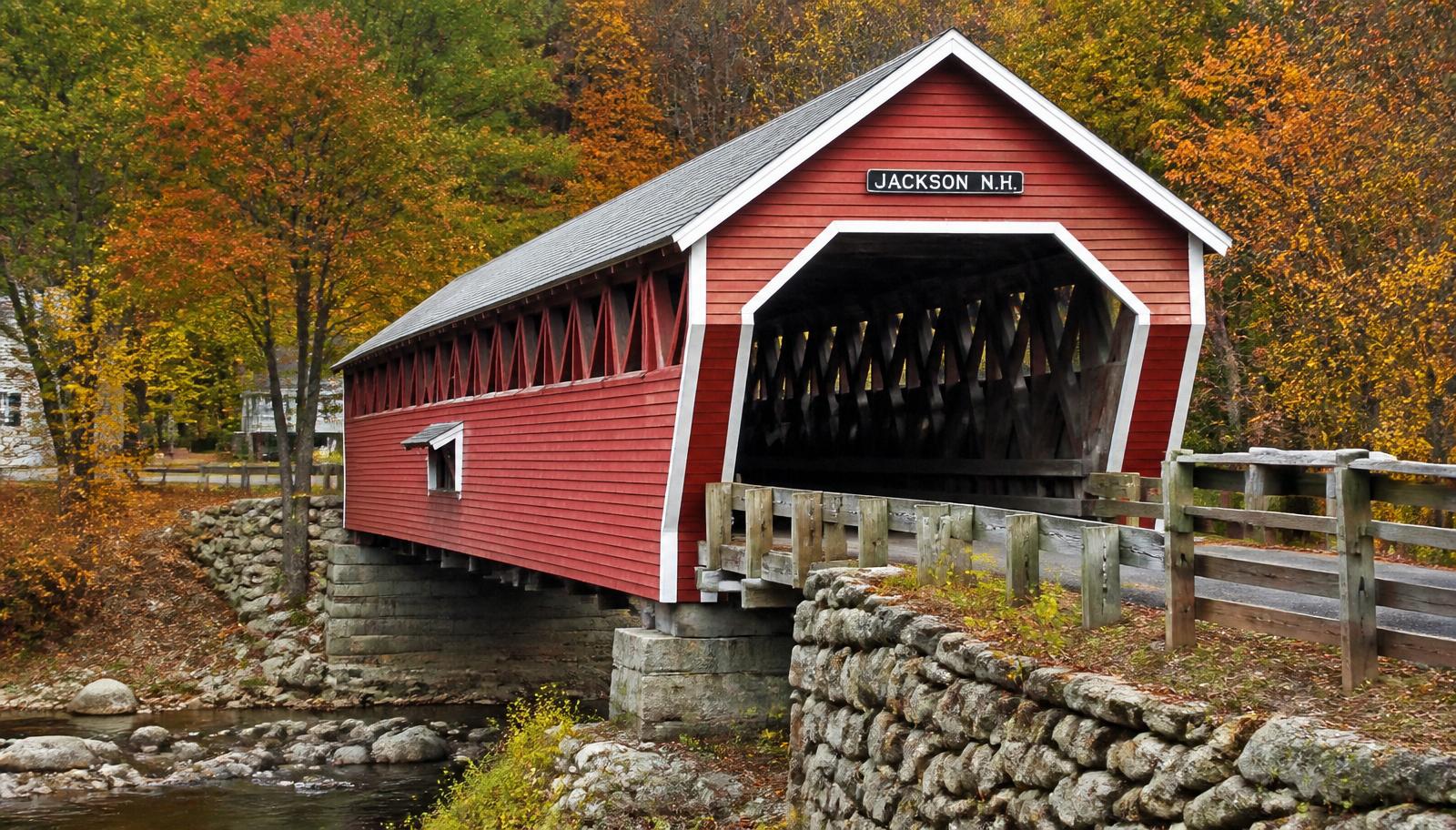 Red-painted New England covered wooden bridge over a rocky stream in autumn