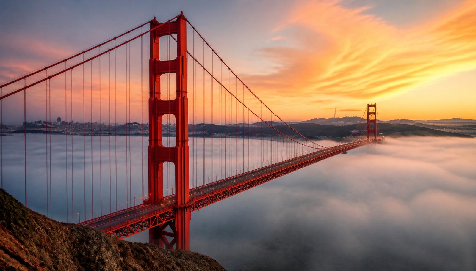 Golden Gate Bridge at sunrise with fog rolling beneath the deck and the Marin headlands beyond